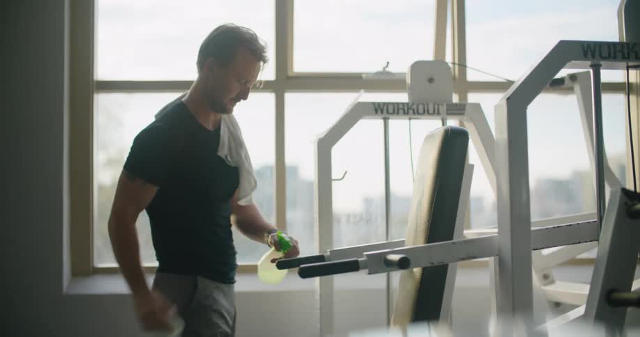 Man cleaning gym equipment with a spray bottle and a cloth
