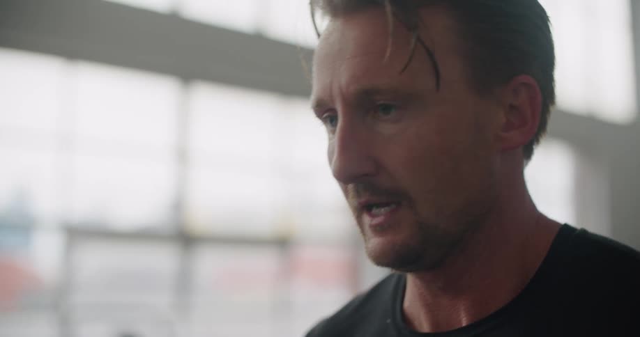 Man exercising next to windows breathes deeply and wipes his sweaty forehead before jogging on treadmill