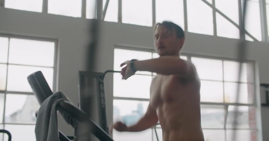 A man in a gym running on a treadmill with equipment and windows in the background