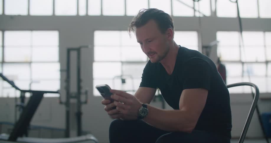 Man sitting on a chair in the middle of a gym using a smartphone