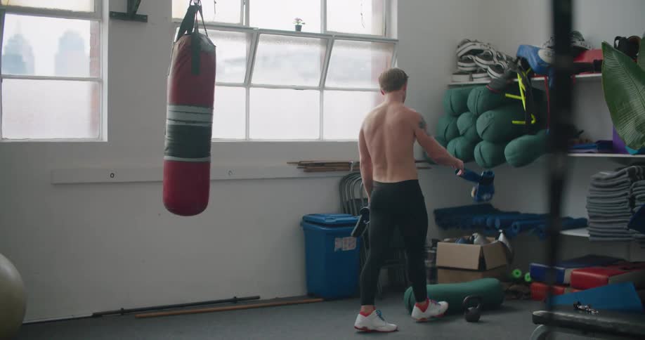 A man picks up boxing gloves and puts them in a box and punches a bag as he walks past