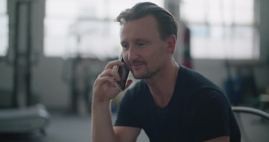 Man sitting on a chair in the middle of a gym talking on the phone