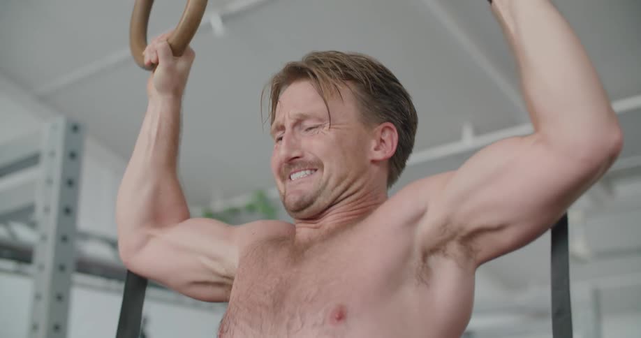A man does pull ups on gymnastic rings and holds a pose before jumping off