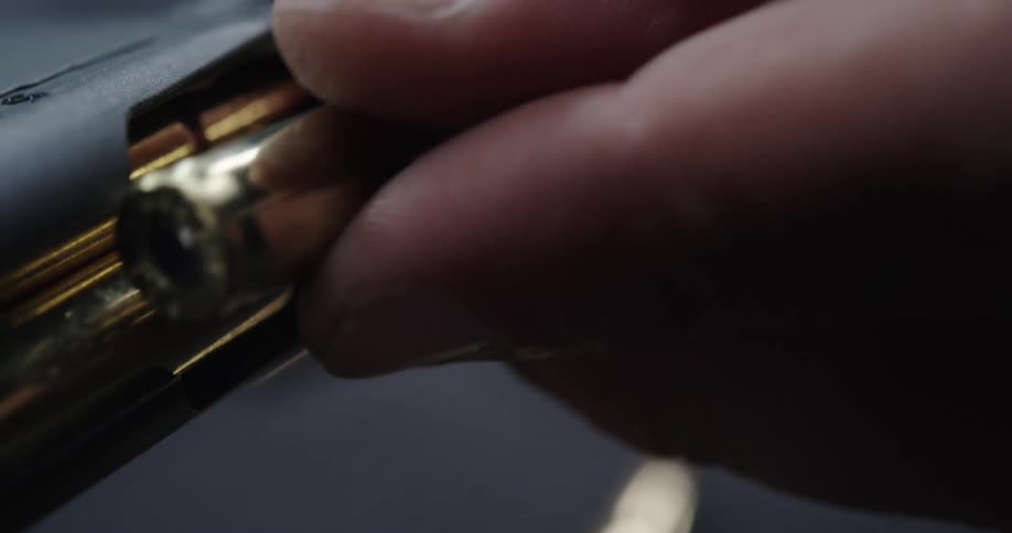A person in a room loading a clip with bullets from a table