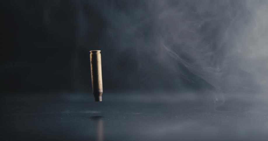 A bullet casing falling to the ground with smoke swirling in the background