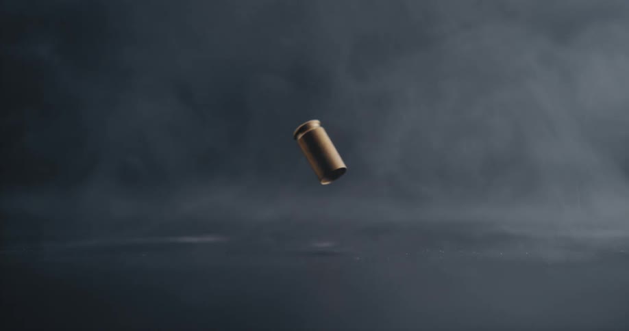 A gold bullet shell casing falls to the floor and bounces then settles on the floor