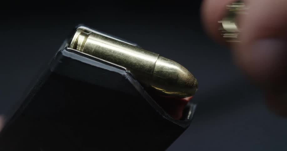 Fingers and thumb load bullets into a magazine