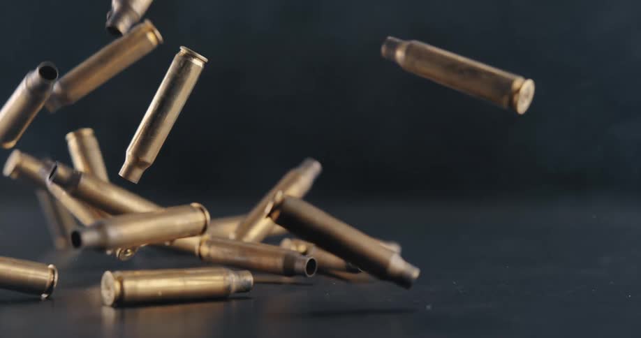 Several spent pieces of ammunition fall downward through a smoky space and land on shiny dark surface