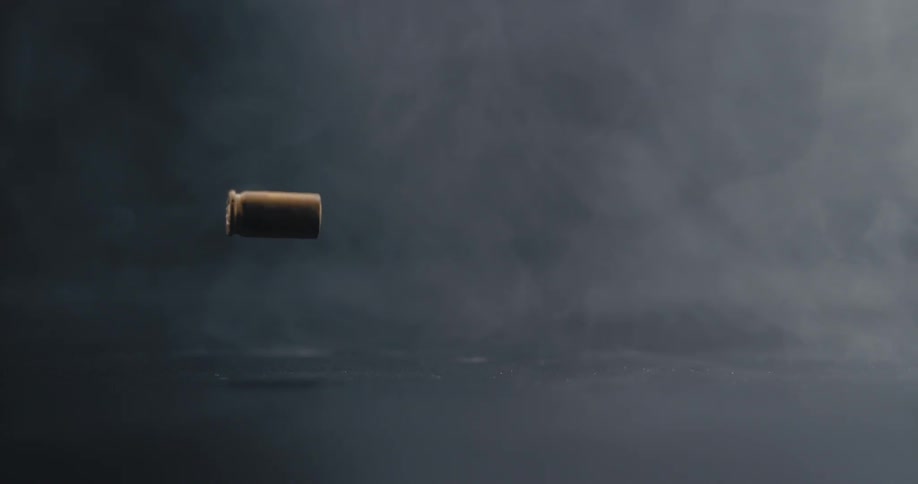 A bullet shell falling to the floor in a room with smoke
