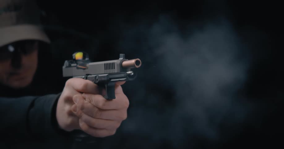 A man fires a hand gun that gives off smoke