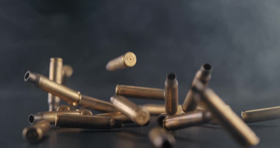 A large number of spent ammunition casings falls downward through a smoky haze
