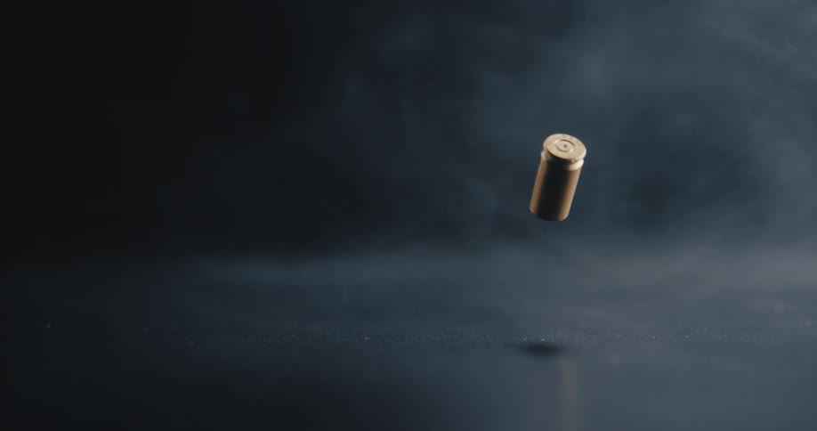 A spent bullet casing slowly falls down and bounces off of a dark and reflective surface