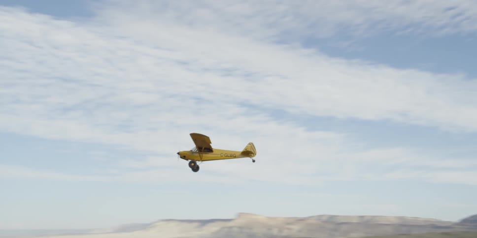 A small yellow single engine plane flying on a cloudy day in the desert
