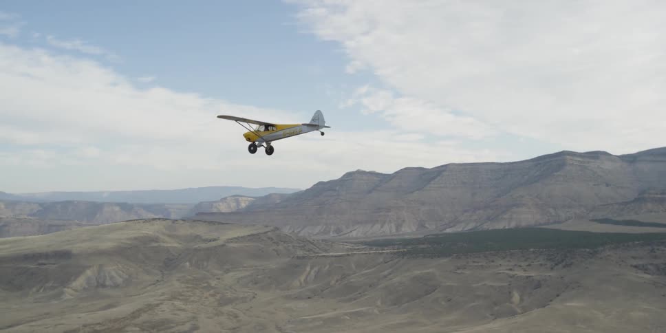 Small yellow plane soaring above some barren land
