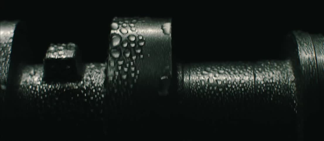 A piece of metal machinery that is wet is spinning in a dark shadowy area