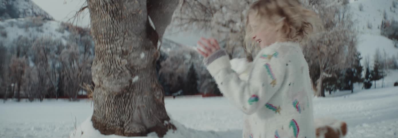 A young blonde girl engaging in a snowball fight outside on a winter day
