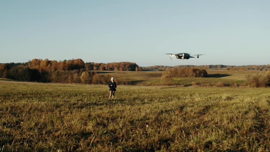Child wearing a knit hat and a jacket is flying a drone in an open field