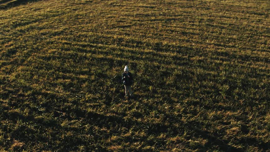 Boy with white wool hat and coat flies a drone in a field