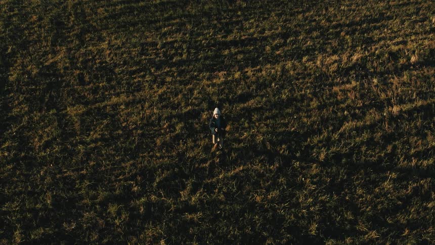 Aerial view of a boy controllinga drone over a field in the countryside at sunset