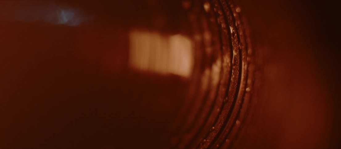 A gray light flashes onto a bronzed metal surface with curved lines