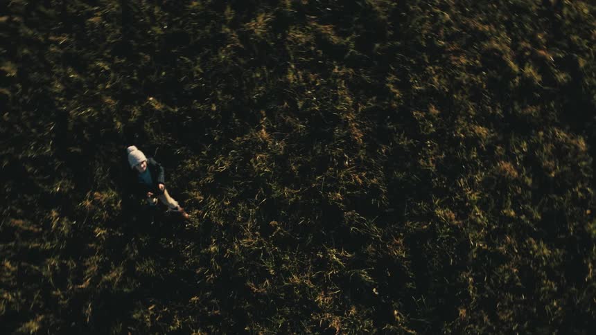 A child holding a remote controller looks up and walks along the grass