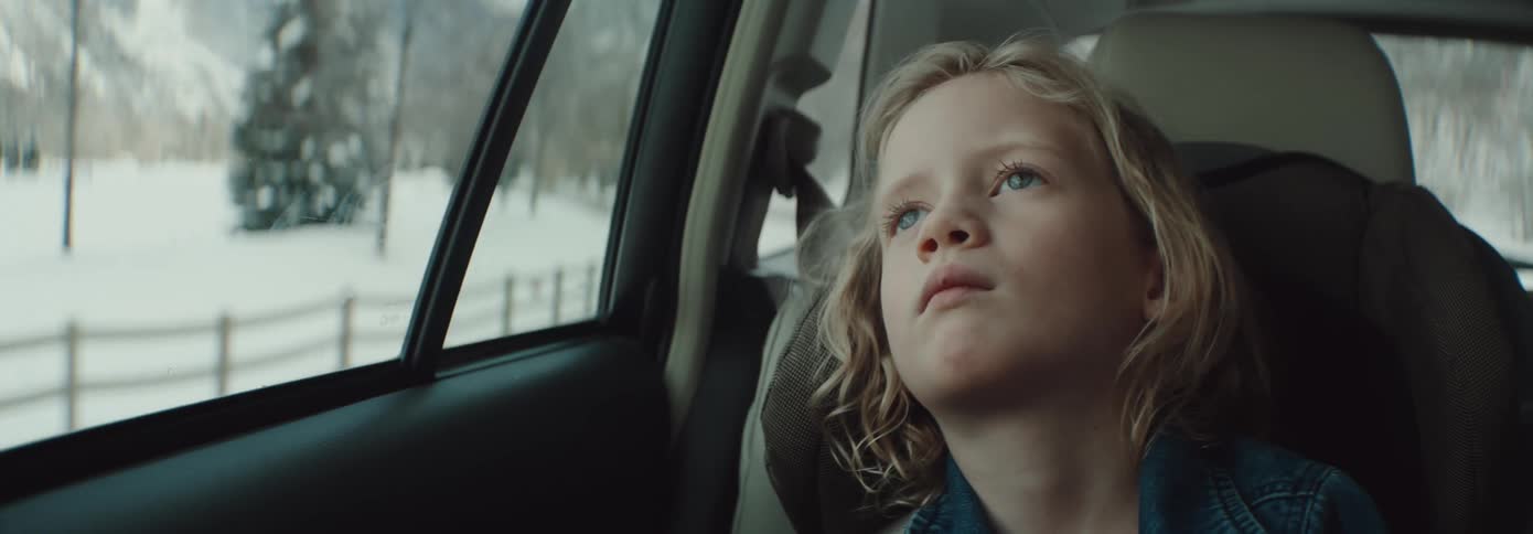 Girl sitting inside a moving car looking out the window at the passing trees