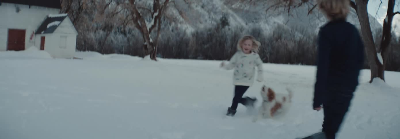 A young boy and girl running around and playing with a pet dog in snow