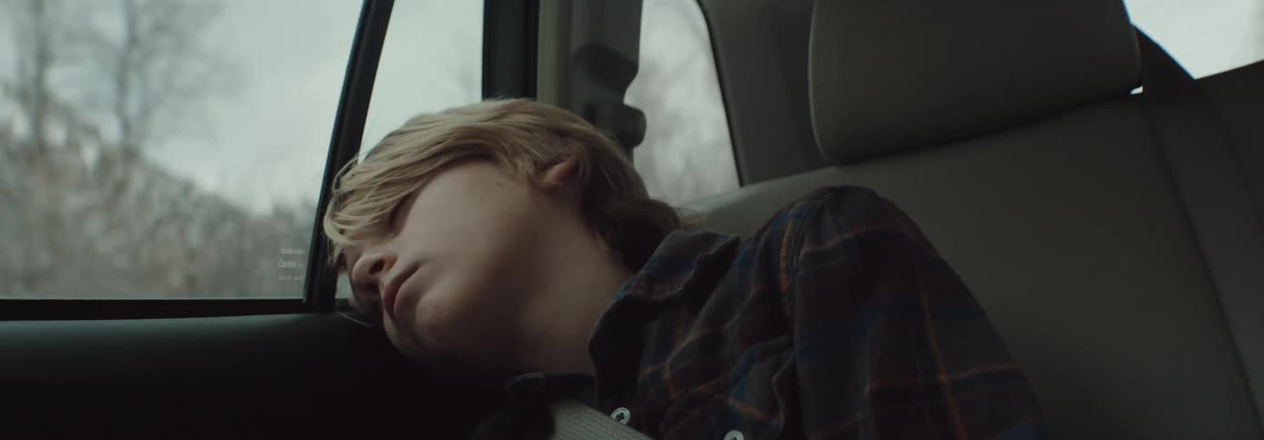 A little boy sleeps in a moving car with his head leaned up against the window