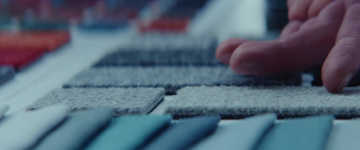 A man slides his hand over the surface of different shades of blue rug samples