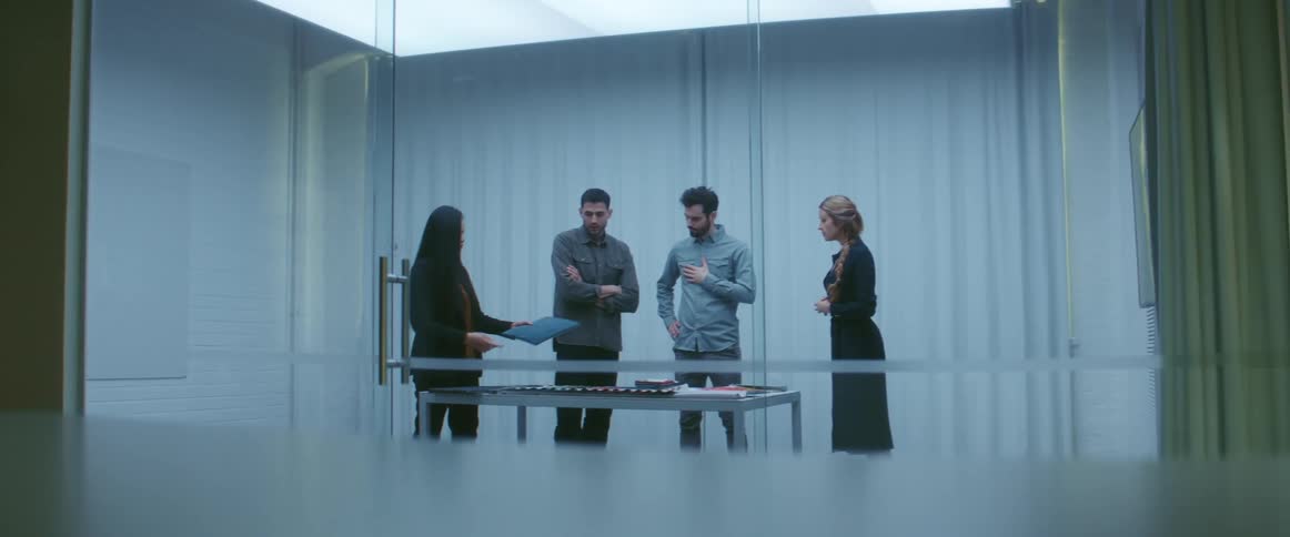 Four people stand talking together in a large office room
