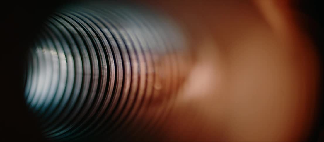 Threaded interior of a cylindrical metallic tube inside a dimly lit room