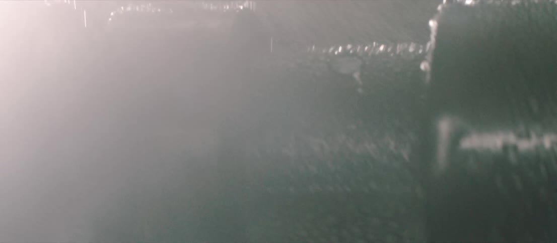 Lightning flashes and rain falls on metal equipment outside at night