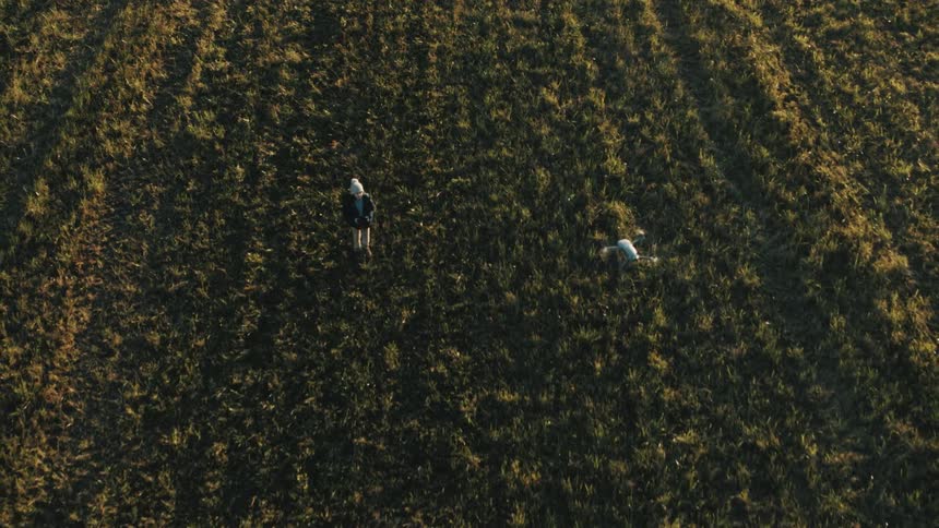 A small boy playing with a drone out in a grass field at daytime