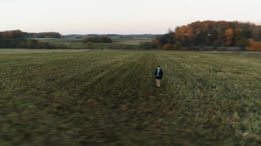 Aerial view of a man standing on the field near a farm piloting a drone
