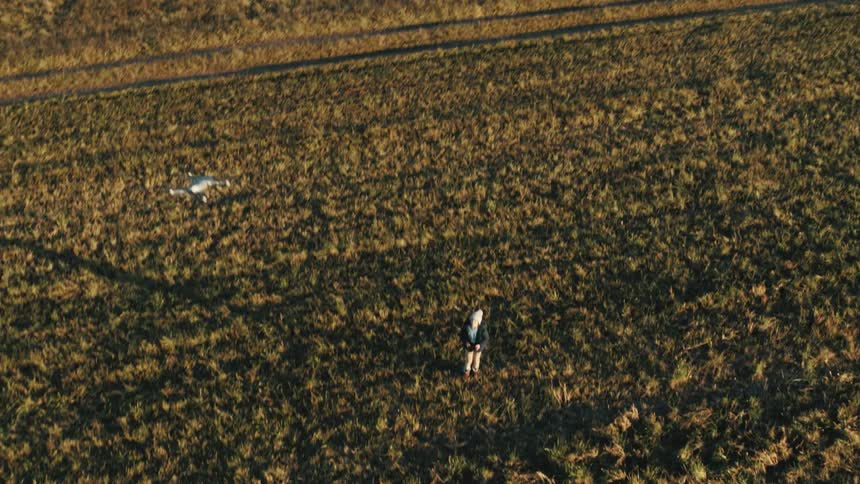 Aerial footage of a small child playing with a drone out in a grass field