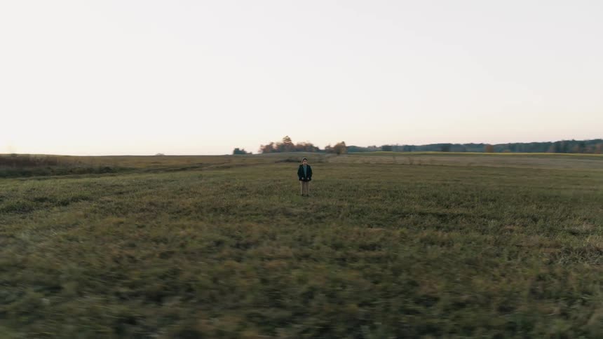 A child wearing a dark jacket is standing in an open field looking around