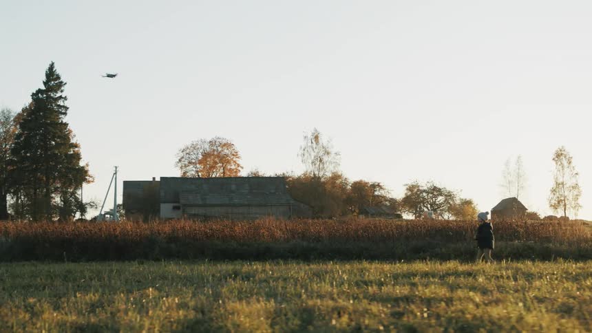 A young boy walks in a rural area and flies a toy airplane