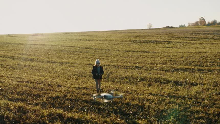 Child wearing a knit hat and a jacket is following a drone as it flies over a field