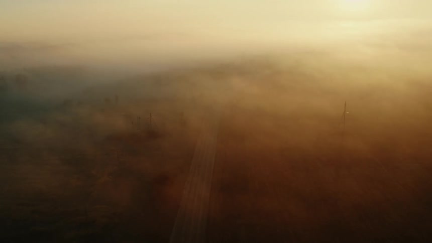 A car driving down a road on a misty day with the sun rising over the horizon