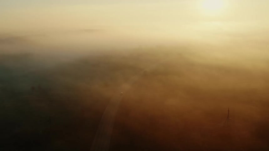 An aerial view of a car traveling on a rural road on a foggy day
