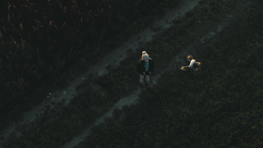 A boy flies a drone in a large open field near crops