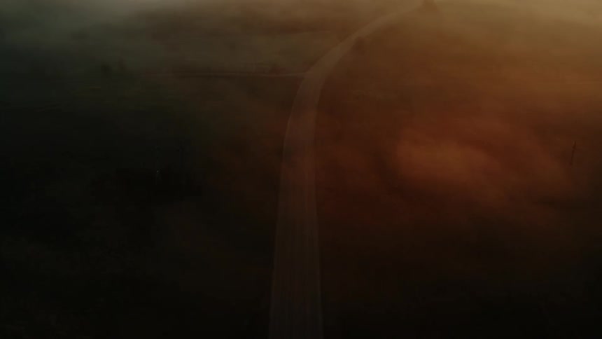 Aerial view of a car driving along a road in the fog at sunset