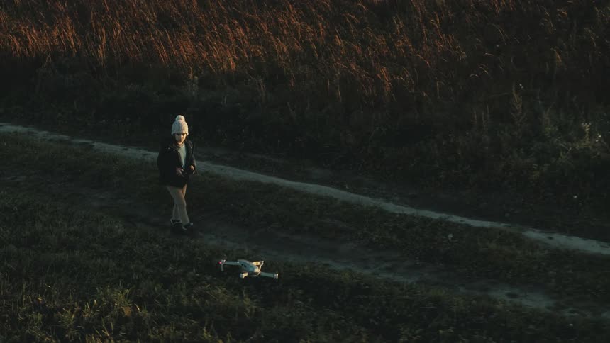 A child flying a drone while walking through a rural field on an autumn day