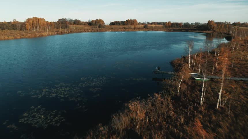 A person standing on a dock next to a pond