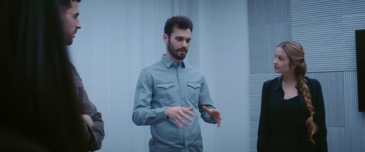 A man speaks to a group of people standing with him around a table indoors