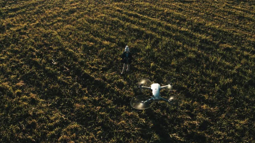A drone is flying in the air as a child stands in an open field