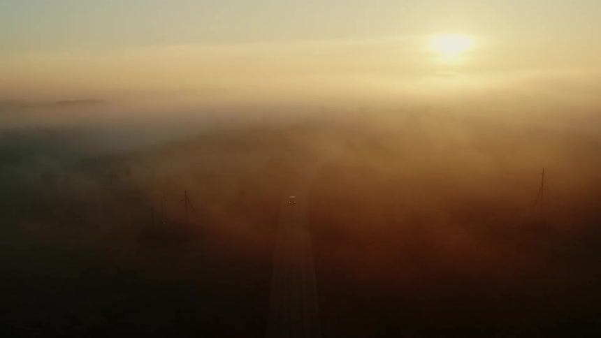A car travels on a road with the sun in a hazy orange sky