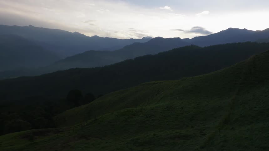 Green grass hills nestle against forest and mist covered mountains
