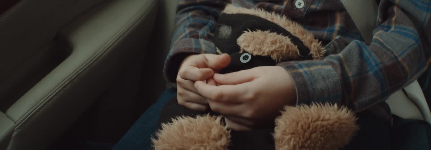 A person sitting in a vehicle with their seatbelts on with a stuffed toy on their lap
