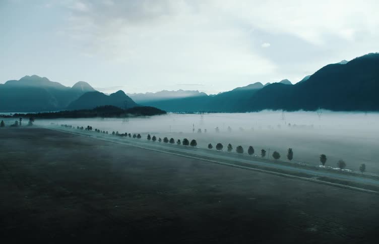 Lake lined with trees and a mountain range in the distance under a cloudy sky